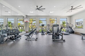 Ein modernes Fitnessstudio mit verschiedenen Trainingsgeräten, großen Fenstern und Blick auf Palmen sowie Gebäude.