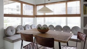 A dining area with a table and chairs, a bowl of fruit, and large windows with blinds. - 2 Bedroom Steps 2 Sand Oceanview Beach Retreat (Marina del Rey)