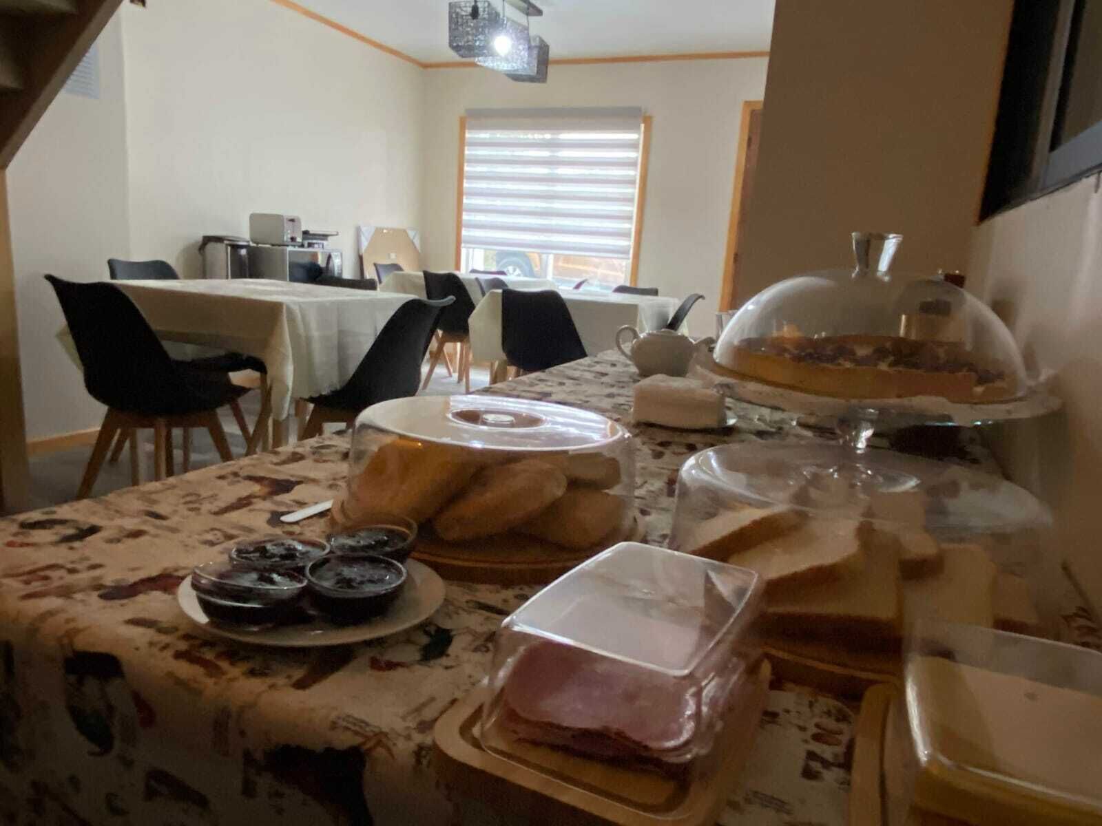 A dining area with tables set for breakfast, including bread, pastries, and a covered dessert display.