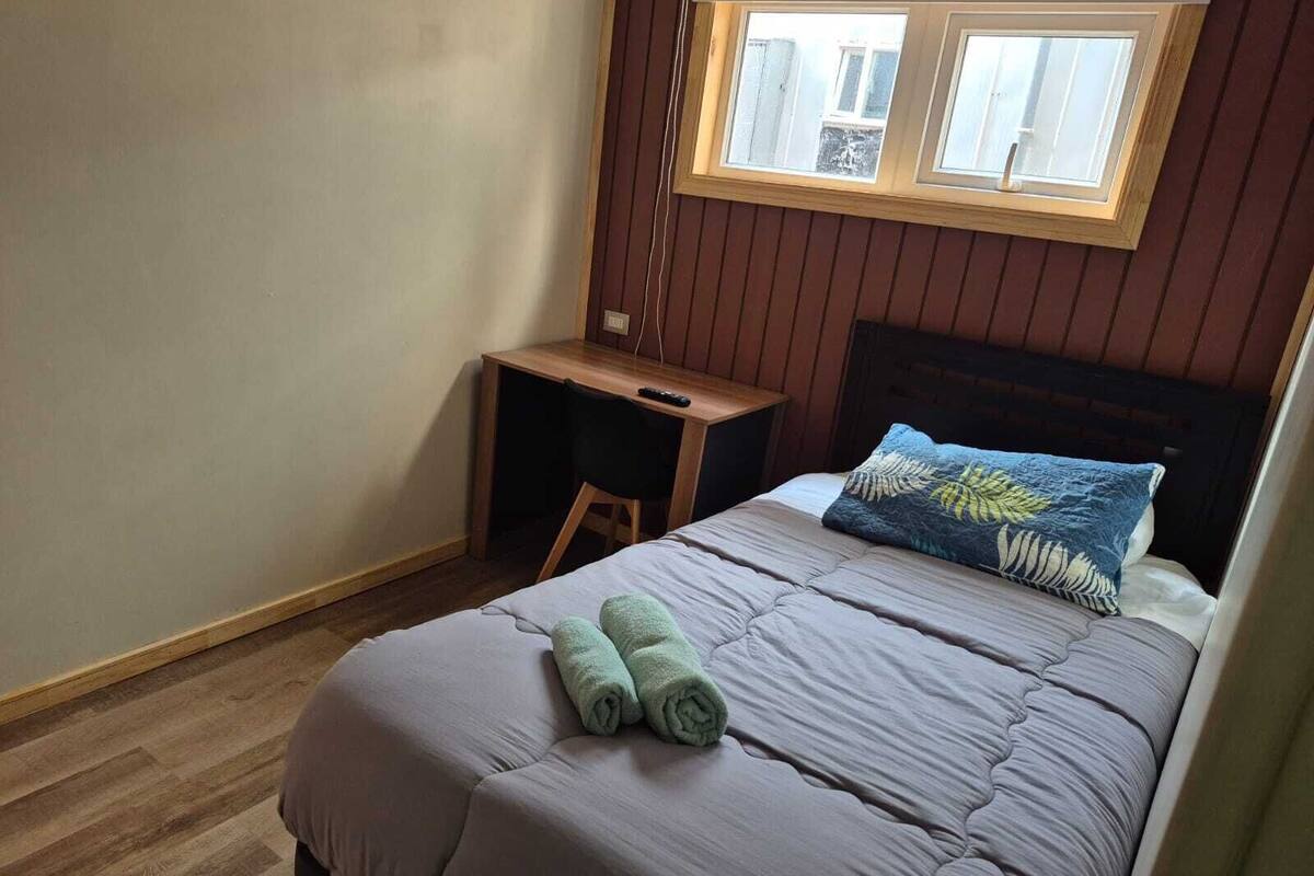 Un dormitorio con cama, escritorio y ventana.