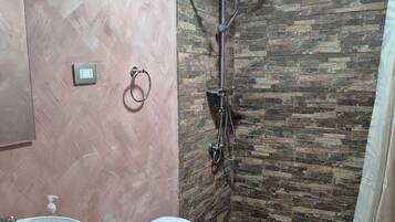 A bathroom with a stone shower wall, a wooden vanity, a white toilet, and a large sink.