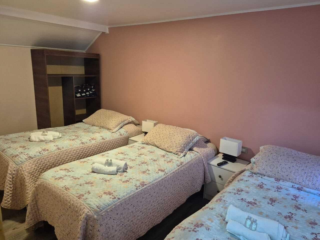 Una habitación de hotel con dos camas, un armario, una mesita de noche y una lámpara.