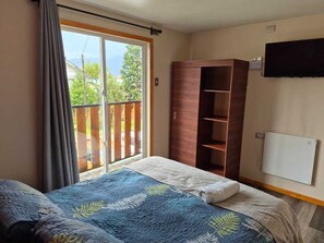 Un dormitorio con cama, armario, televisor y puerta corrediza de vidrio a un balcón.