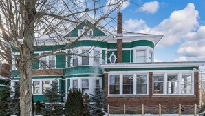 A two-story house with a green and white exterior, a brick chimney, and a fenced yard.