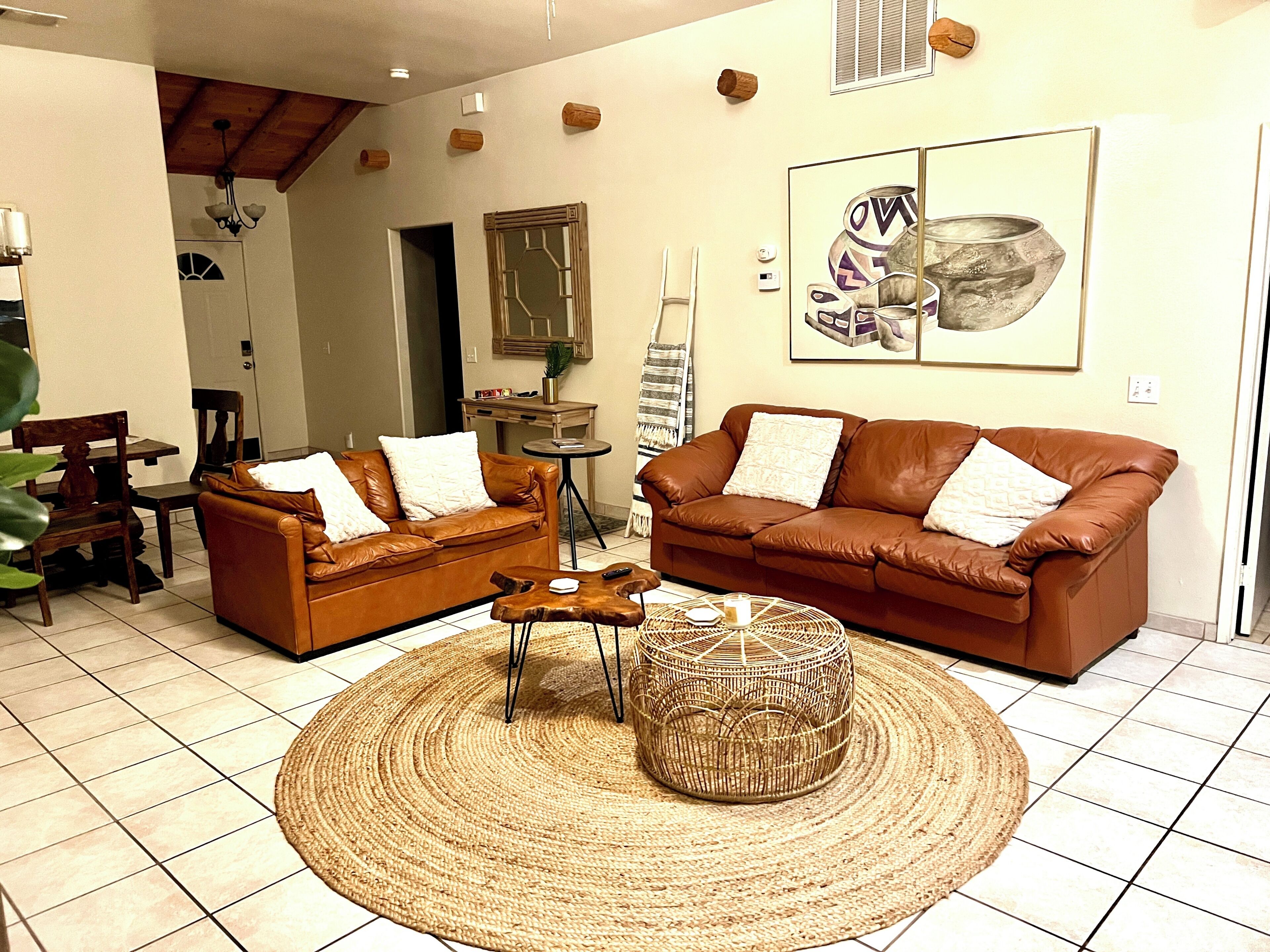 A living room with two brown leather sofas, a round woven ottoman, a small round table, and a large painting on the wall.