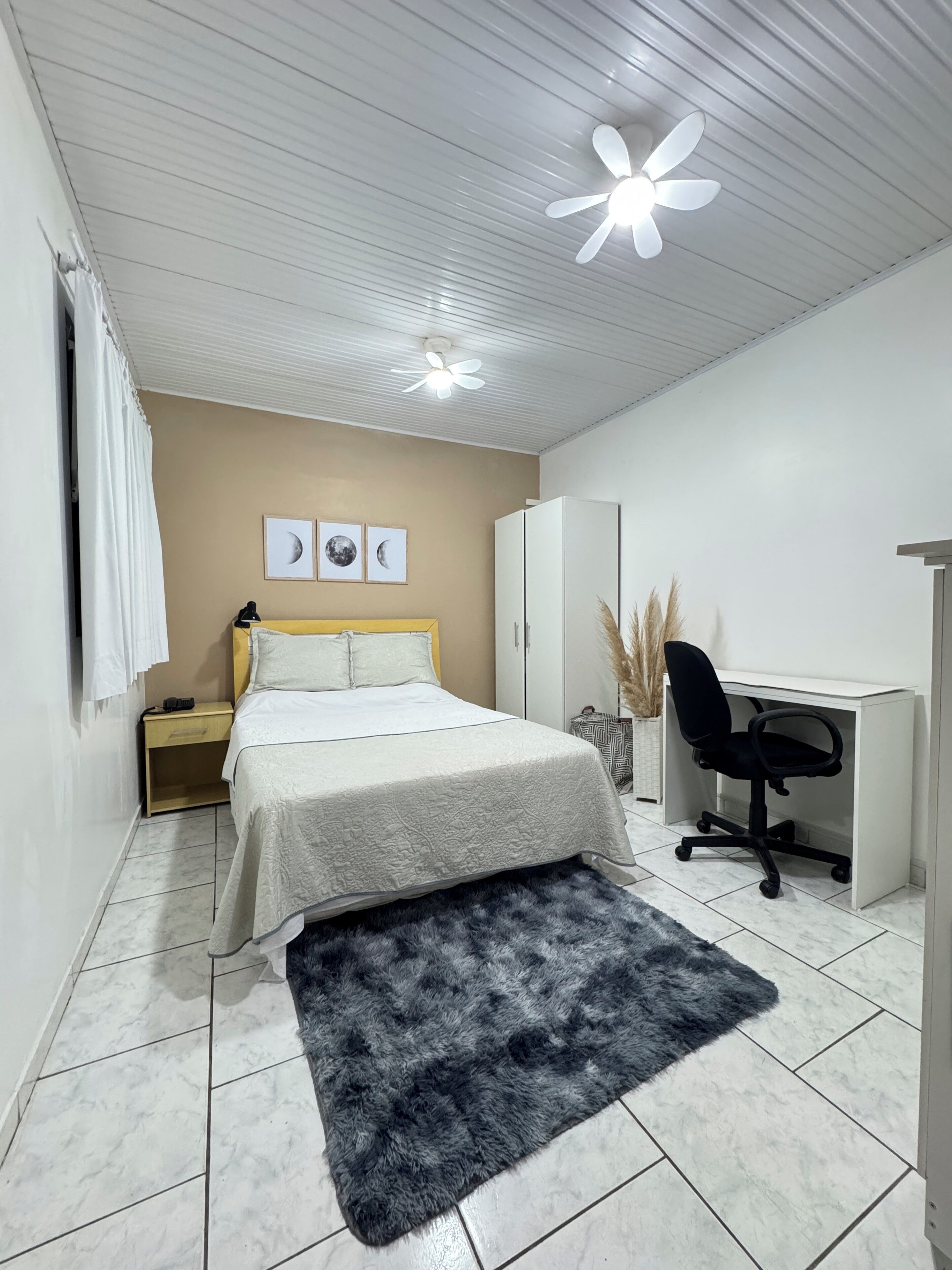 Un dormitorio con cama, escritorio, silla, armario y ventilador de techo.