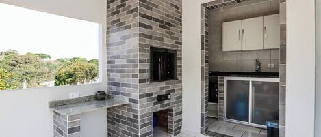 Una cocina moderna con chimenea de ladrillo, armarios blancos y un amplio ventanal con vistas al verdor.