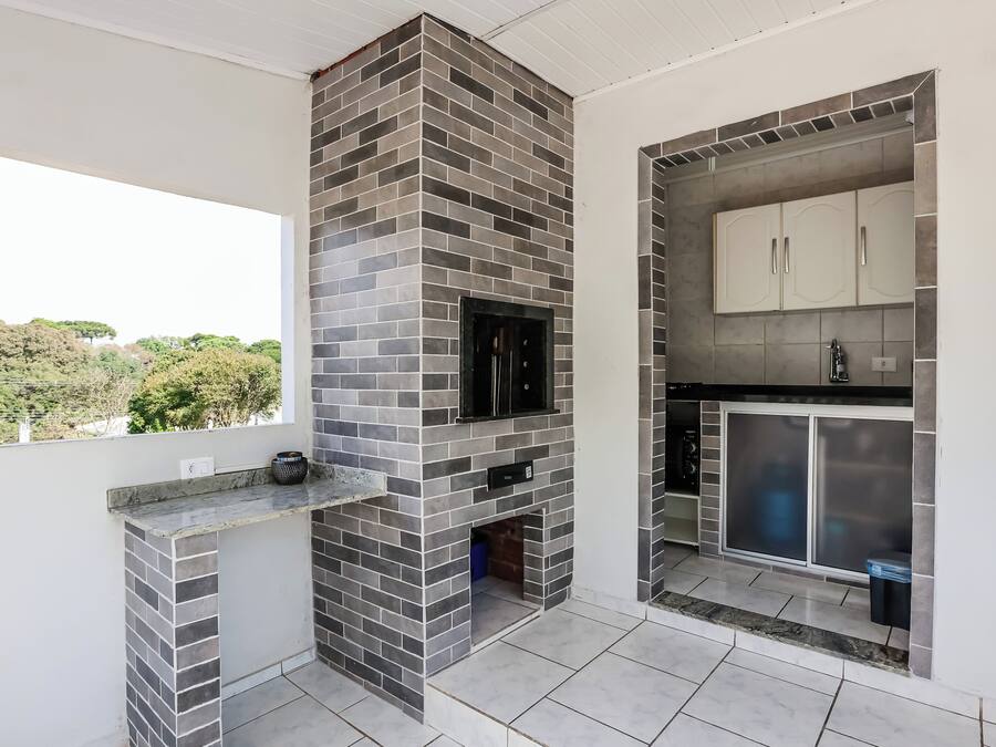 Una cocina moderna con chimenea de ladrillo, armarios blancos y un amplio ventanal con vistas al verdor.