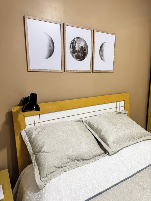 A bed with a headboard, two pillows, a bedside lamp, and three framed pictures of the moon on the wall.