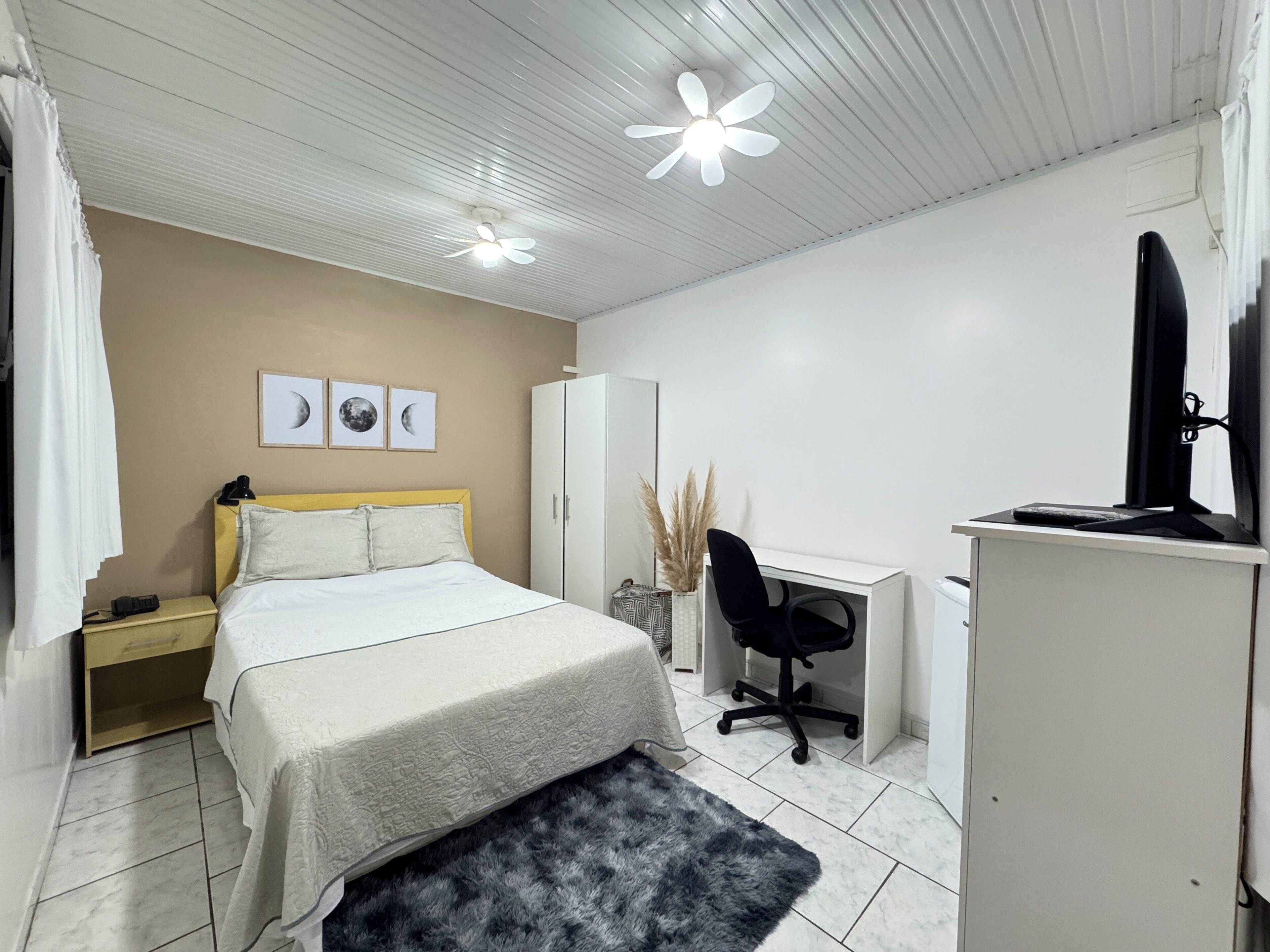 A bedroom with a bed, a desk, a chair, a wardrobe, and a television.