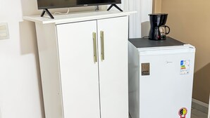 Un meuble blanc sur lequel est posée une télévision à écran plat, un petit réfrigérateur et une machine à café sur une table.