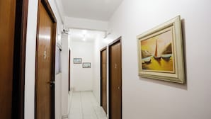 Un couloir avec des portes en bois, numérotées 2, 3 et 5, qui donnent sur des pièces. Un tableau encadré représentant des bateaux est accroché au mur.