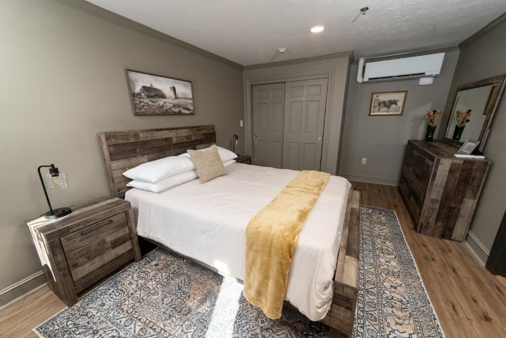 Un dormitorio con cama, mesita de noche, cómoda y un ventanal grande.