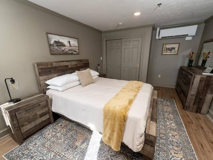 Un dormitorio con cama, mesita de noche, cómoda y un ventanal grande.