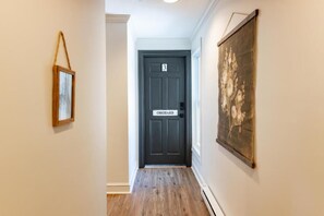 Un pasillo con una puerta oscura que dice '3 ORCHARD', un cuadro enmarcado a la izquierda y una gran obra de arte floral a la derecha.