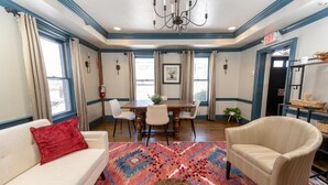 Una sala de estar con sofá, sillón, mesa de comedor, sillas y alfombra estampada.