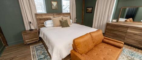 Un dormitorio con una cama, un aparador de madera, un sofá marrón y una alfombra estampada.