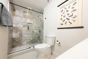 A bathroom with a glass shower enclosure, a toilet, and a wall-mounted poster of bird types. - The Inn at Fireside Tavern Sherborn (Sherborn)
