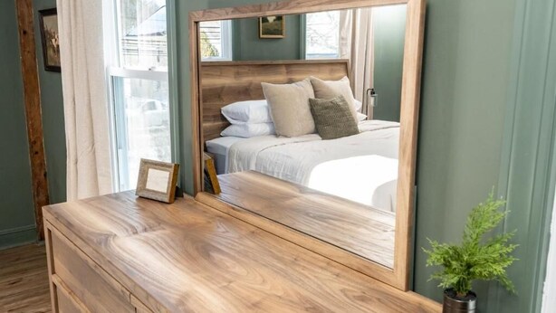 Un dormitorio con un espejo grande, cómoda de madera y una planta en maceta.