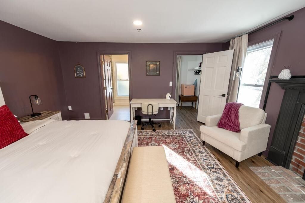 A bedroom with a bed, desk, chair, and a fireplace.