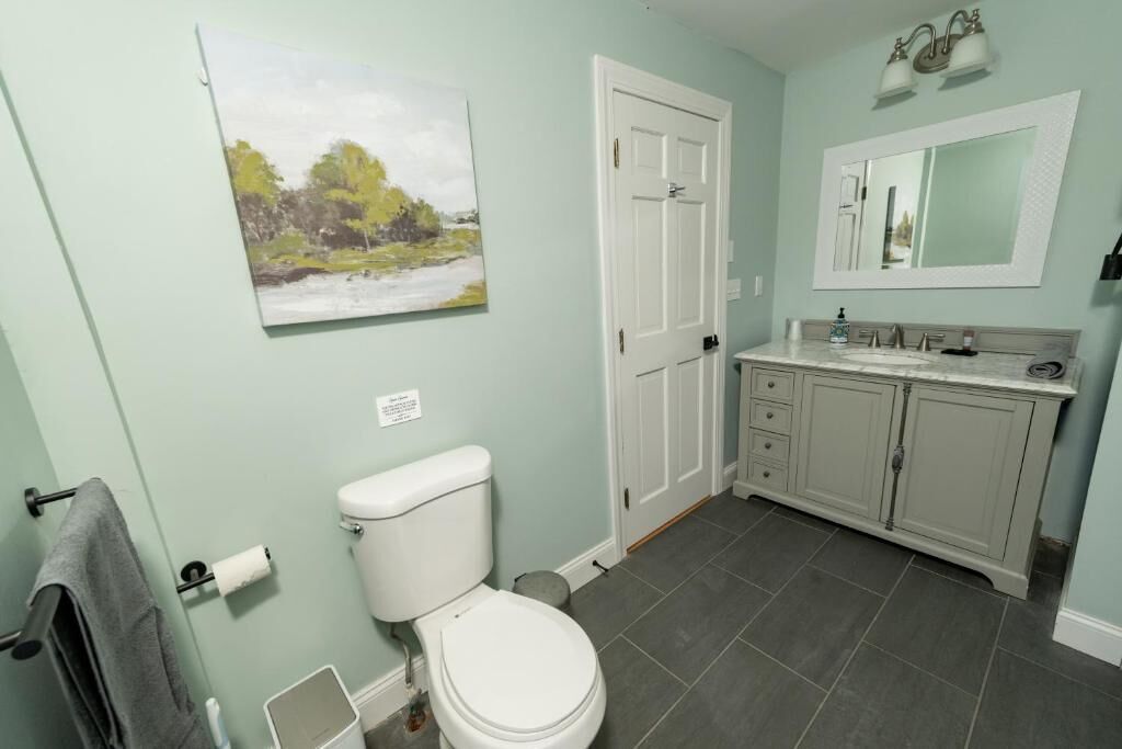 Une salle de bain comprenant des toilettes, un lavabo, un meuble et un tableau accroché au mur.