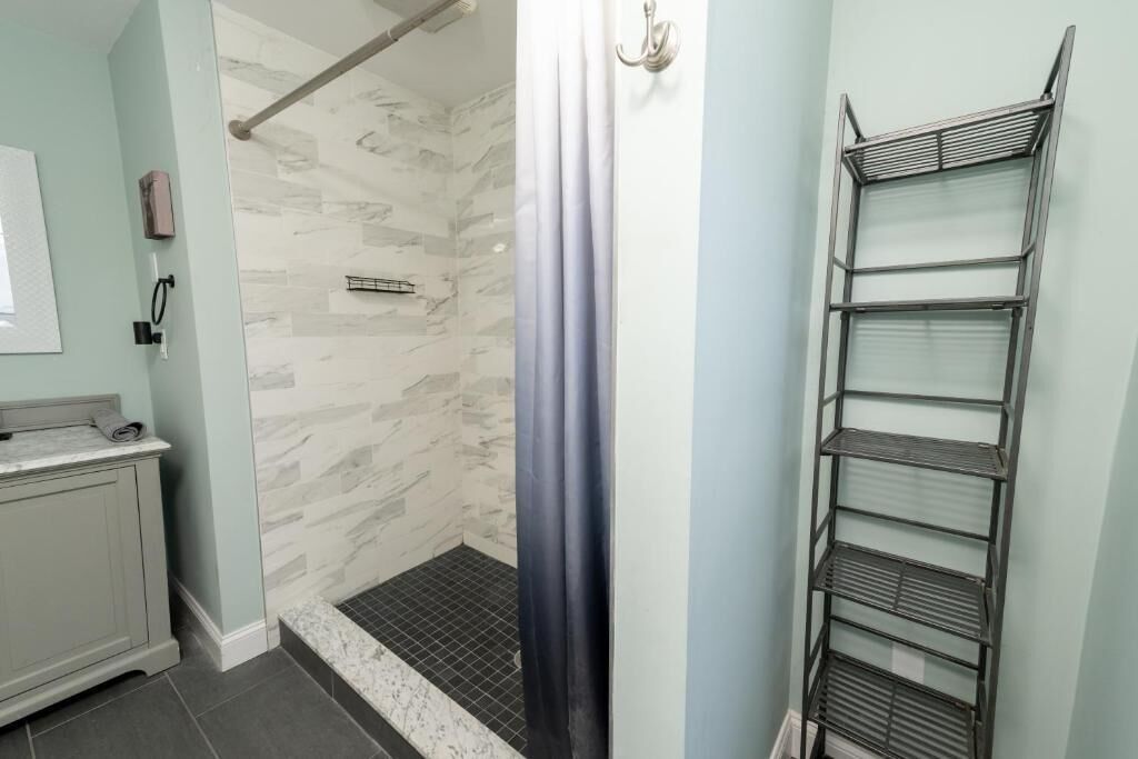 A bathroom with a shower, a towel rack, and a metal shelf unit.