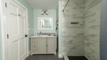 A bathroom with a white vanity, a mirror, a shower with a glass door, and a tiled floor.