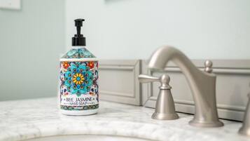 Un baño con encimera de mármol, un grifo y una botella de jabón para manos Blue Jasmine.
