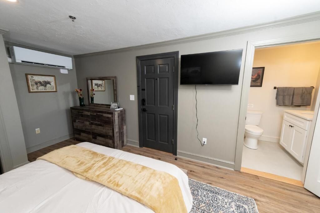 Ein Schlafzimmer mit Bett, Kommode, Fernseher und einem durchgegangene Tür erkennbaren Badezimmer.