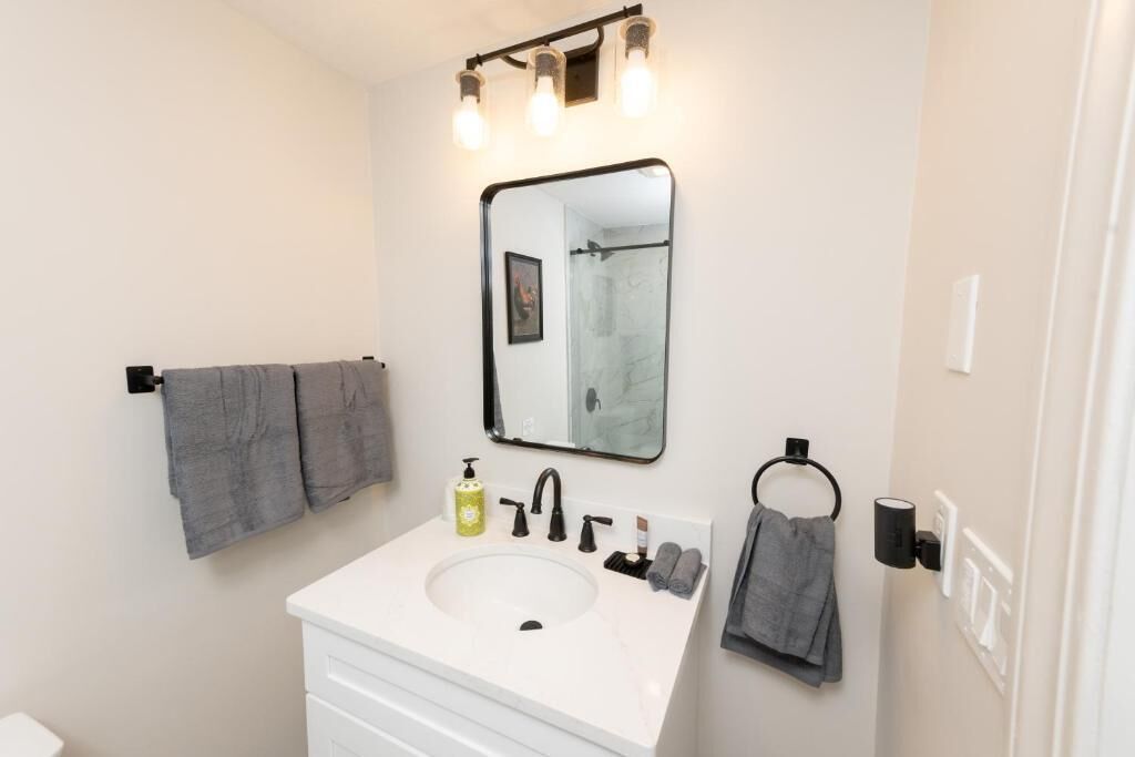 A bathroom with a white sink, black faucet, and a mirror with lights above it.