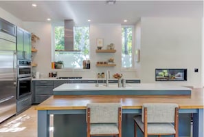 A modern kitchen with a central island, built-in appliances, and a large window. - Luxury Designer House w/ Pool, Gym & Sauna (Austin)