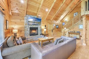 A log cabin interior with a stone fireplace, wooden walls, a sofa, a coffee table, and a staircase.