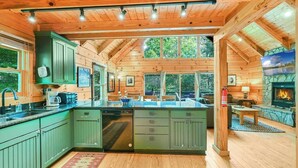 A log cabin with a kitchen featuring green cabinets, a stone fireplace, and large windows. - Lake Lure Lodge in the Trees Sleeps Eight (Lake Lure)