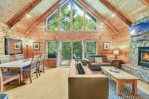 A log cabin interior with a dining area, sofa, fireplace, and large windows.