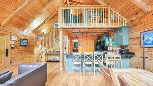 A log cabin with a loft bedroom, a kitchen with teal cabinets, and a dining area with wooden chairs. - Lake Lure Lodge in the Trees Sleeps Eight (Lake Lure)