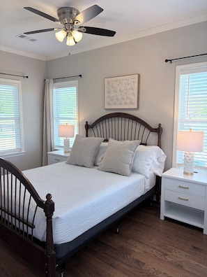 A bedroom with a wooden bed, white bedding, a ceiling fan, bedside lamps, and a window with blinds.