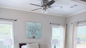 A bedroom with a bed, a ceiling fan, a nightstand, a lamp, a painting, and windows with curtains. -  Deer Sanctuary Pasture Views & Total Relaxation (Statham)