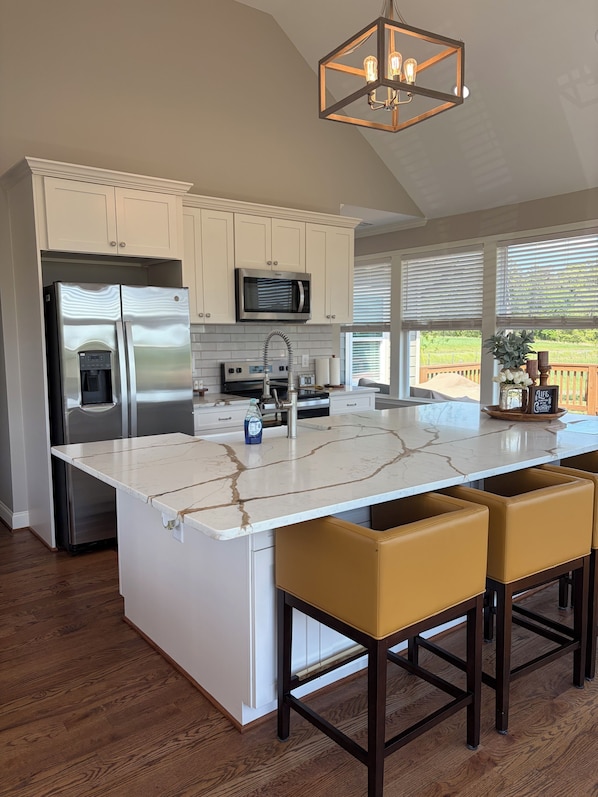 A kitchen with a marble island, stainless steel appliances, and a pendant light.