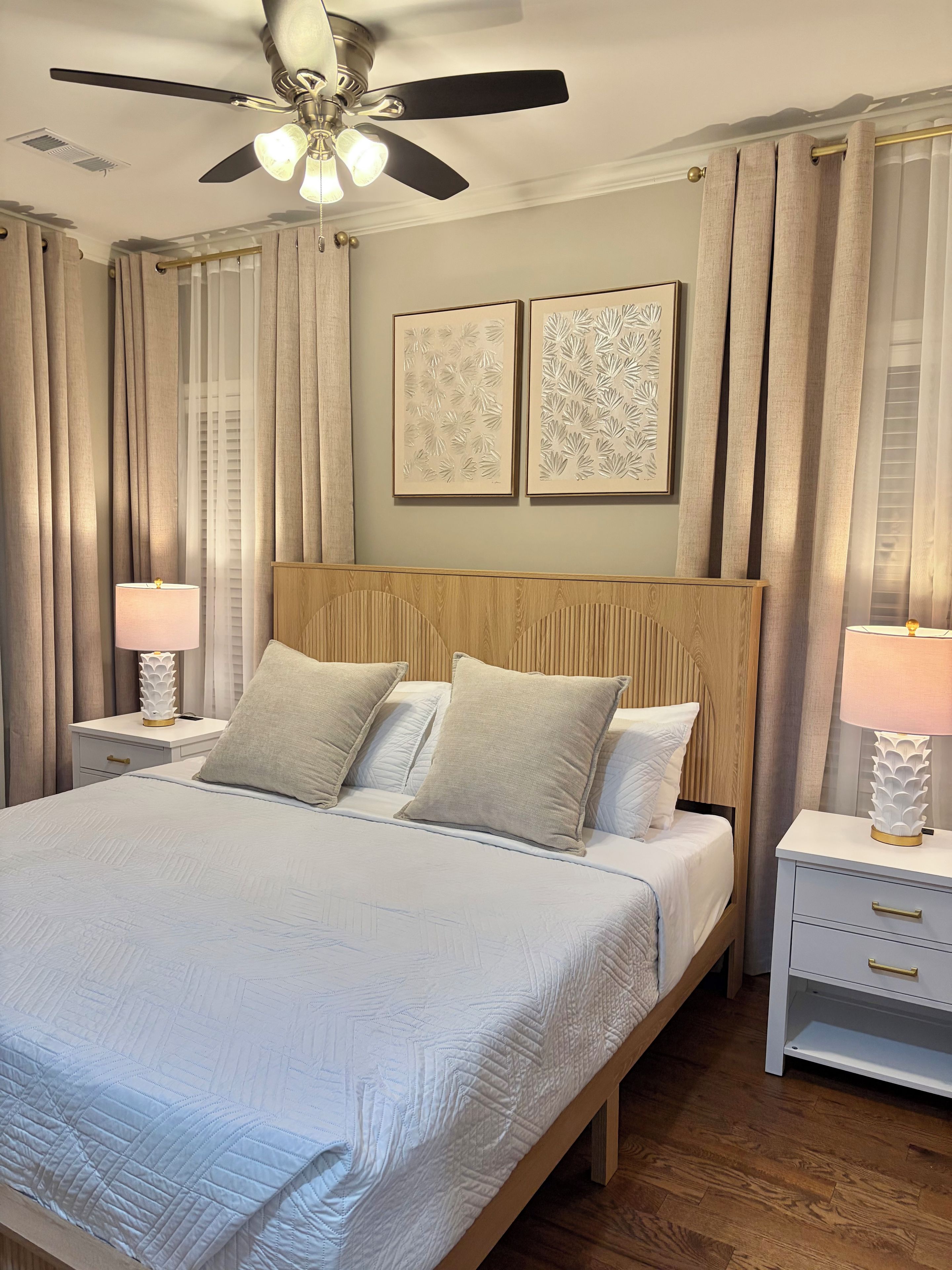 Un dormitorio con cama, mesitas de noche, ventilador de techo y cortinas.