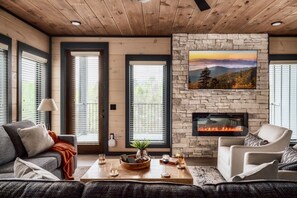 A cozy living room with a stone fireplace, a sofa, a coffee table with drinks, and a large window with blinds. - FREE Waterpark/IndoorPool/HotTub/GameRoom/Sleeps18 - Sunset Ridge (Sevierville)
