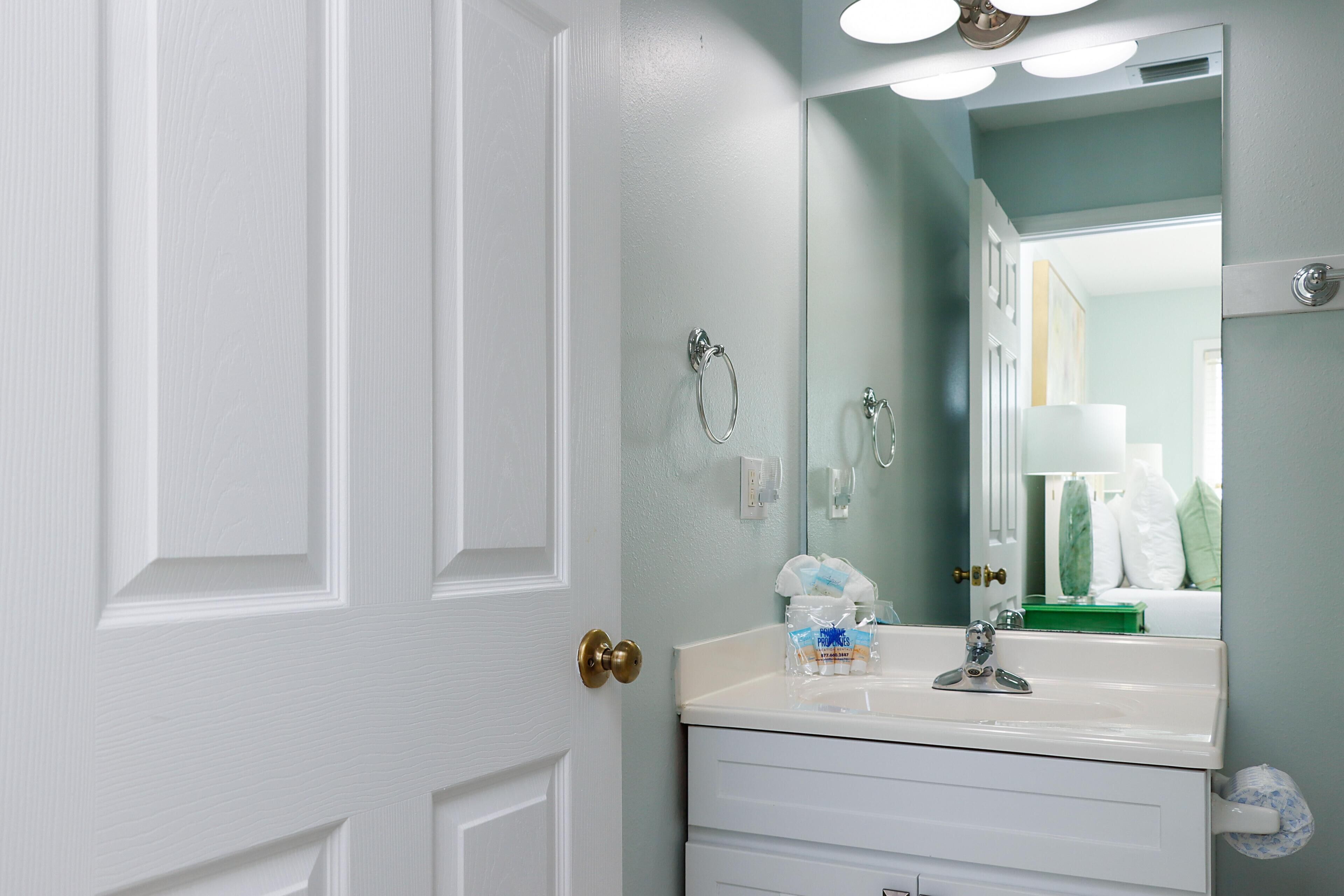 A bathroom with a white door, a mirror, a sink, and a towel rack.
