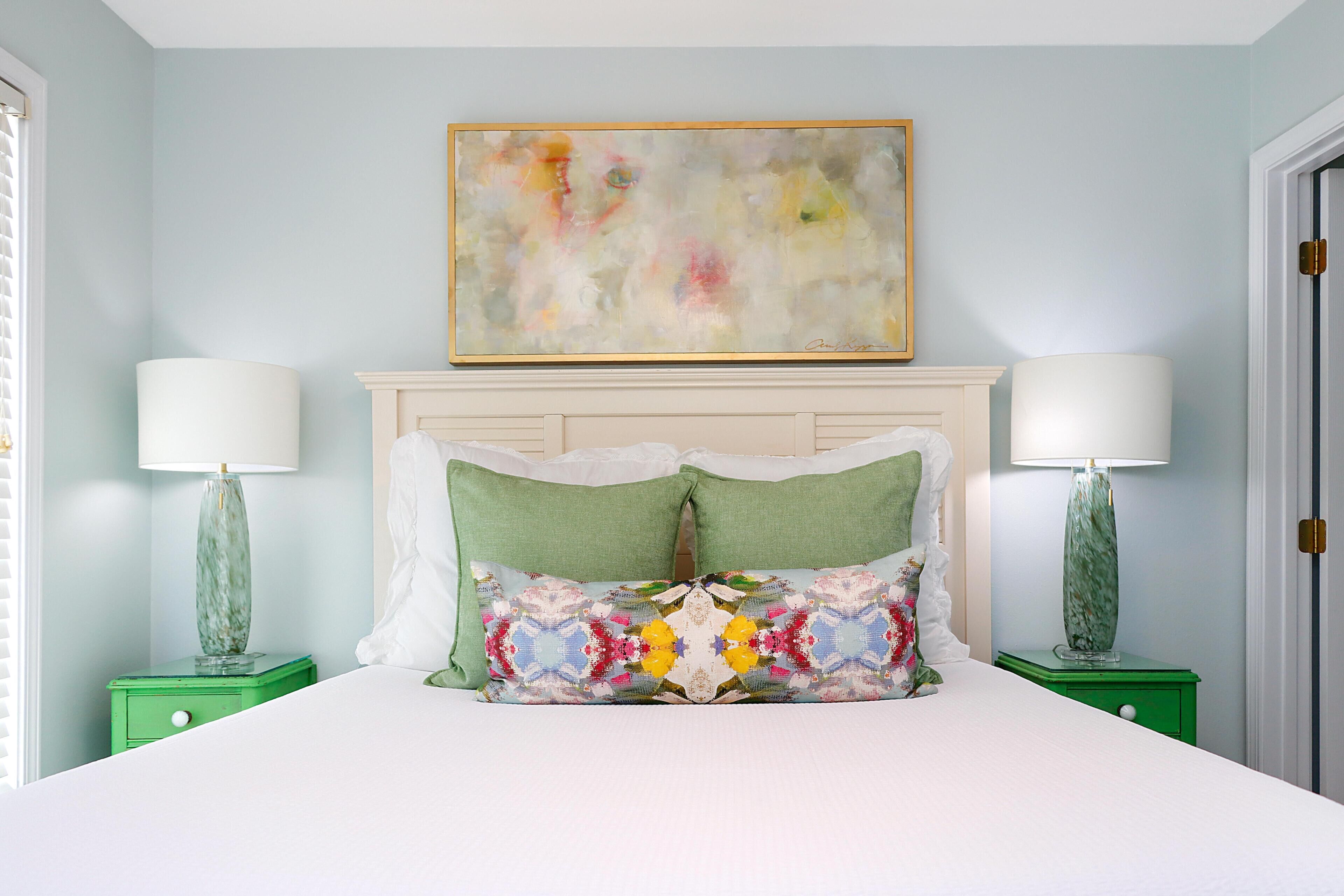 A bedroom with a bed, two nightstands, a painting, and a door.