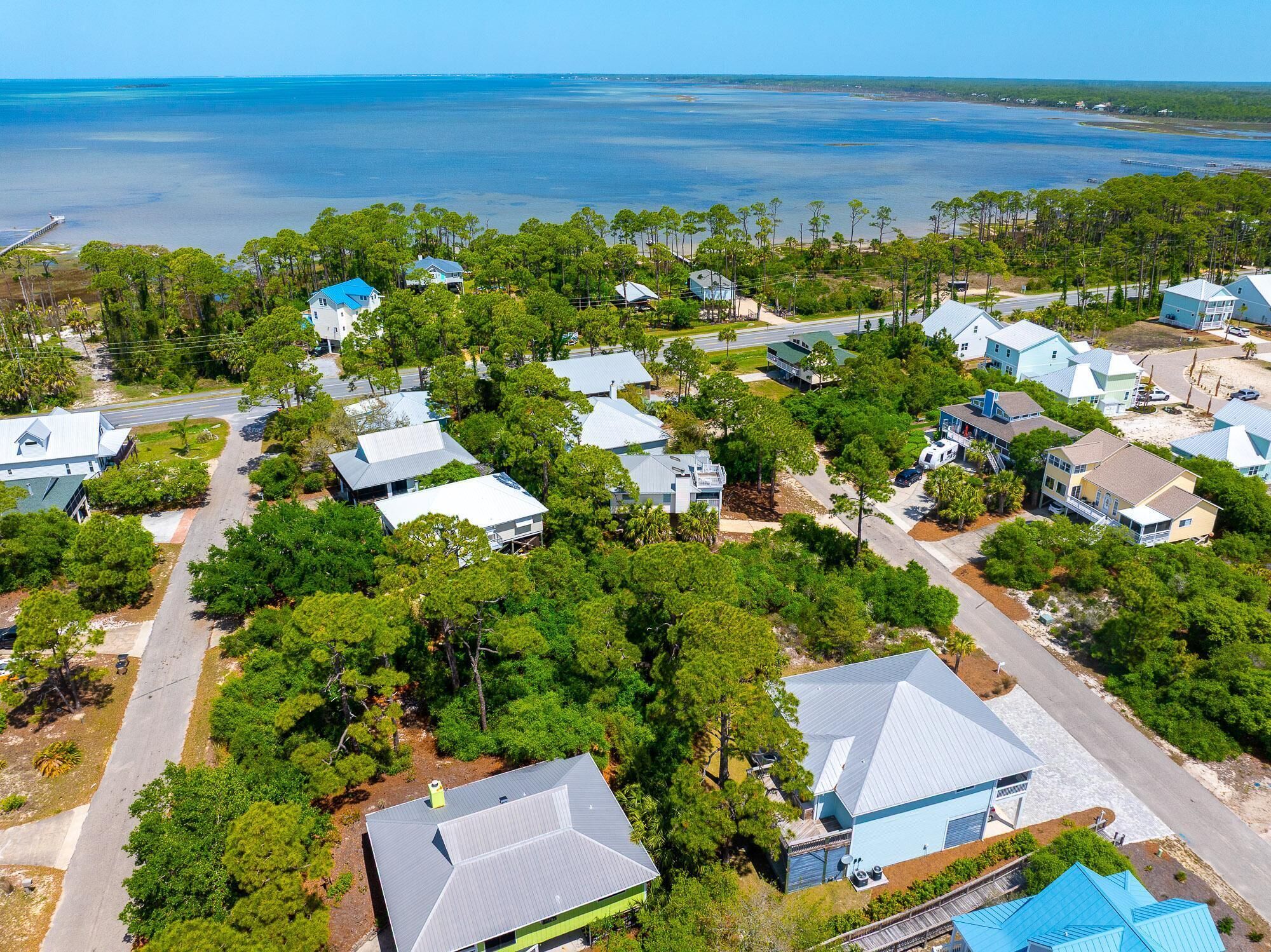 An aerial view of a coastal residential area with houses, roads, and a pier extending into the water.