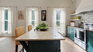 Una cocina con una isla central, una zona de comedor con sillas y vistas al exterior a través de grandes ventanales.