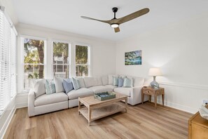 A living room with a sectional sofa, a coffee table, a wooden floor, a ceiling fan, and a painting on the wall. - New Listing! 105 Grand Pavilion - Remodeled! (Isle of Palms)