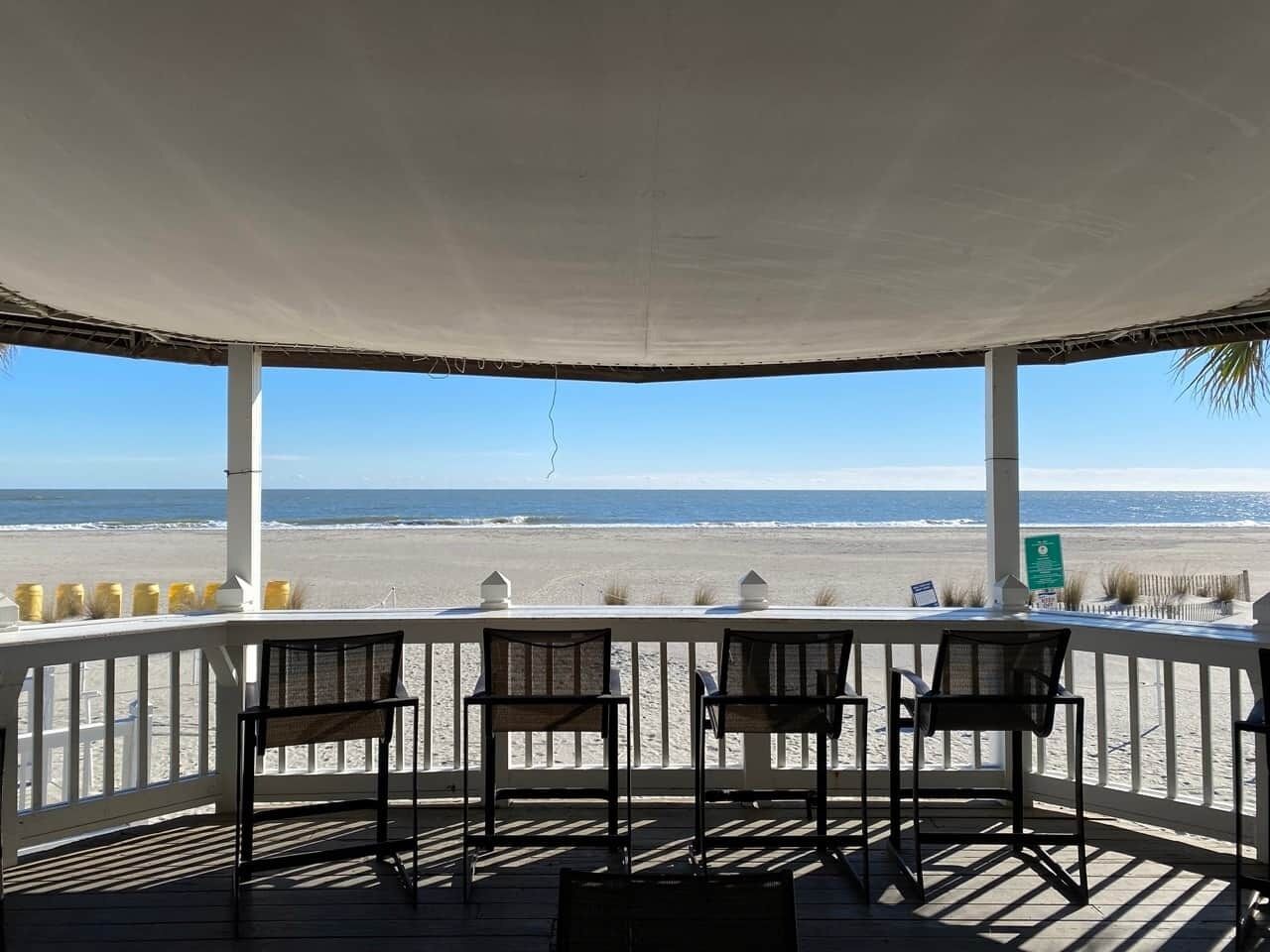 A covered outdoor seating area with a view of the beach.
