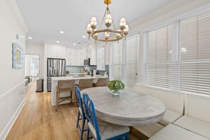 A modern kitchen with white cabinets, a stainless steel refrigerator, and a round dining table with blue chairs. - New Listing! 105 Grand Pavilion - Remodeled! (Isle of Palms)
