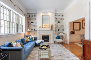 A living room with a blue sofa, a fireplace, and bookshelves. - The Riverview | 1 Block to River St (Savannah)