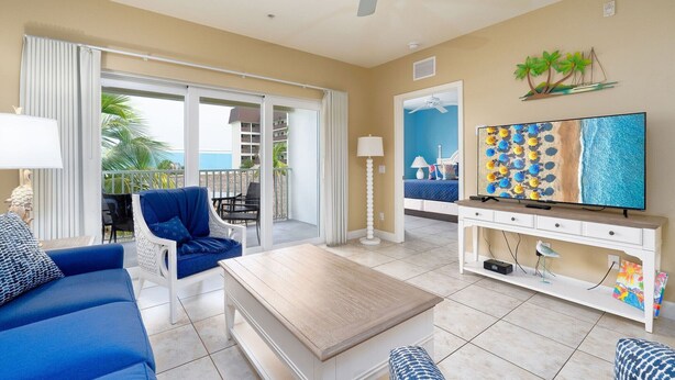 A living room with a sofa, armchair, coffee table, TV, and a balcony with a view. - Harbour House #305 "Island Time Harbour" (Fort Myers Beach)