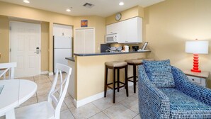 A compact kitchen with a microwave, stove, and refrigerator. There is a dining area with a white table and chairs. A blue patterned sofa is against the wall. - Harbour House #305 "Island Time Harbour" (Fort Myers Beach)